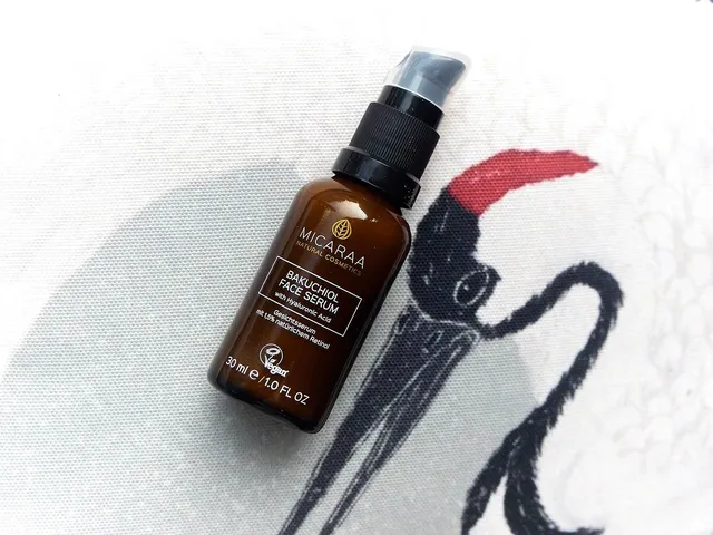 Das Bakuchiol Face Serum von MICARAA liegt in einer dunkelbraunen Glasflasche auf einem Kissen mit einem Kranich-Motiv.